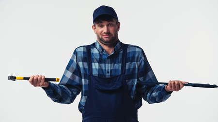 Confused repairman in overalls holding tools isolated on white