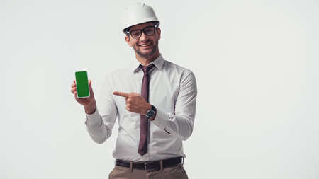 Cheerful engineer pointing at smartphone with chroma key isolated on whiteの写真素材