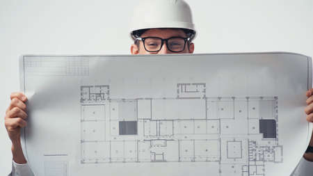 Blueprint in hands of architect in eyeglasses and helmet isolated on whiteの写真素材