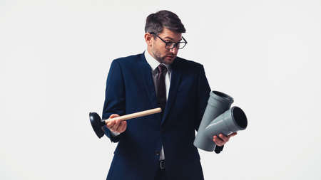 Confused manager in suit holding plastic pipe and plunger isolated on whiteの写真素材
