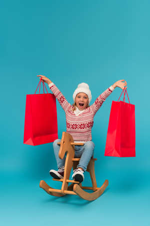 excited girl with shopping bags riding rocking horse on blueの写真素材