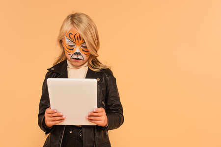 girl with tiger face painting using digital tablet isolated on beige