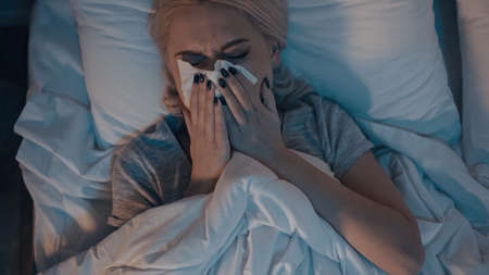 Top view of woman suffering from runny nose on bedの写真素材
