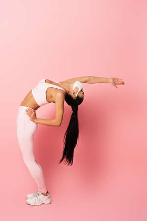 young sportswoman in medical mask stretching back on pinkの写真素材