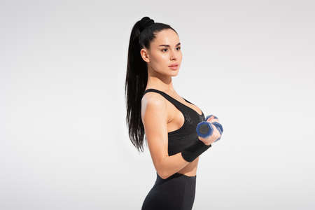 strong sportswoman in sportswear exercising with dumbbells isolated on gray
