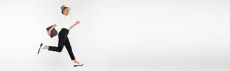 smiling african american businesswoman with paper folder running in air isolated on white, bannerの写真素材