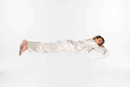 full length view of barefoot african american woman in silk pajamas sleeping while levitating...