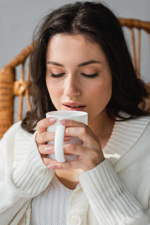 brunette woman in warm cardigan enjoying warm tea with closed eyesの写真素材