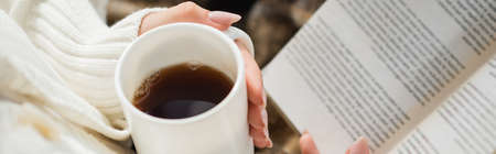 partial view of woman with cup of warm tea and book, bannerの写真素材