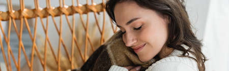 pleased woman with closed eyes holding soft blanket near face, bannerの写真素材