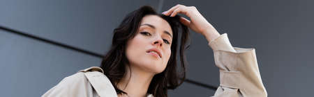 low angle view of brunette woman adjusting hair while looking at camera, bannerの写真素材