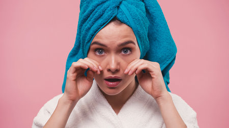 young woman with terry towel on head touching face isolated on pinkの写真素材