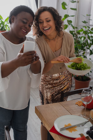 African american mother showing smartphone at cheerful daughter during thanksgiving dinnerの写真素材