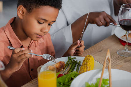 african american boy having thanksgiving dinner near blurred grannyの写真素材