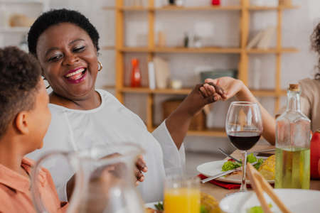 happy african american woman praying with blurred grandson and daughter during thanksgiving dinnerの写真素材
