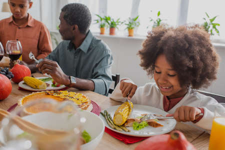 african american girl having thanksgiving dinner near blurred grandpa and brotherの写真素材