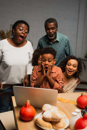 amazed african american boy touching face near laptop and familyの写真素材