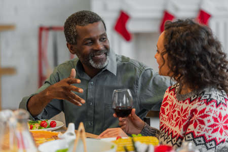 smiling african american man gesturing while talking to daughter during christmas dinnerの写真素材