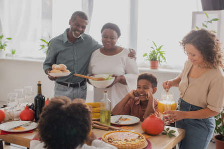 Smiling african american grandparents holding food near family and thanksgiving dinnerの写真素材