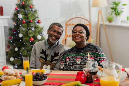 cheerful african american couple near table served with festive dinner and christmas tree on blurred backgroundの写真素材