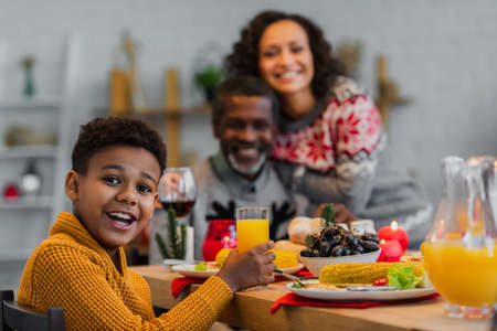 happy african american boy looking at camera during thanksgiving dinner with blurred familyの写真素材