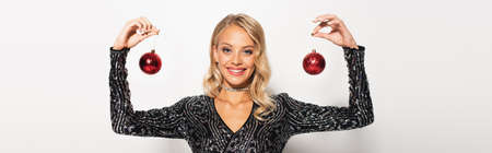 glamour woman in black and shiny blouse holding christmas balls while smiling at camera on white, bannerの写真素材