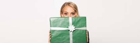 blonde woman obscuring face with green gift box and looking at camera isolated on white, bannerの写真素材