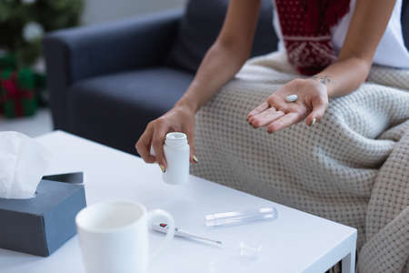 cropped view of sick woman with pill in hand near thermometer and cup of warm drink on blurred table