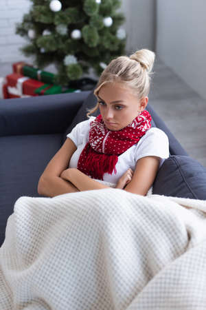 high angle view of sick and upset woman with crossed arms on sofa near christmas tree on blurred backgroundの写真素材