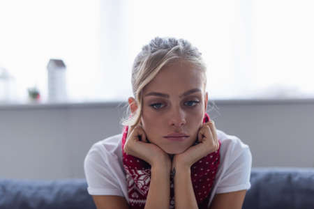 diseased and upset woman in warm scarf sitting at homeの写真素材