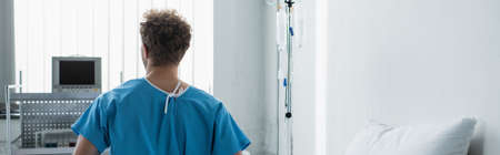 back view of curly man in patient gown sitting on hospital, bannerの写真素材