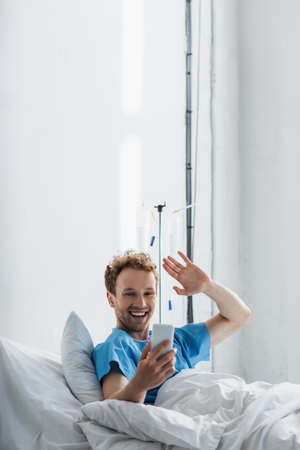 happy patient waving hand while having video call on smartphone in hospitalの写真素材