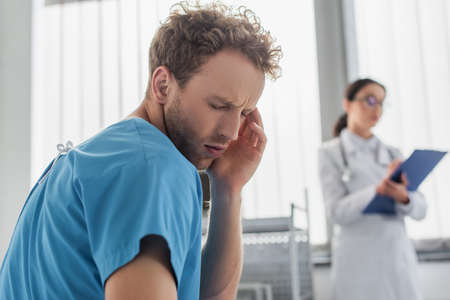 curly patient suffering from headache near blurred doctor in hospitalの写真素材