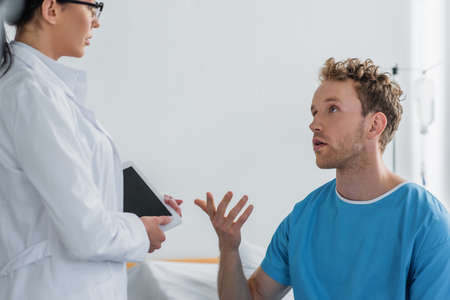 patient gesturing while talking with doctor in white coatの写真素材
