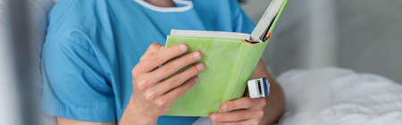 partial view of patient with oximeter on finger reading book in hospital, bannerの写真素材