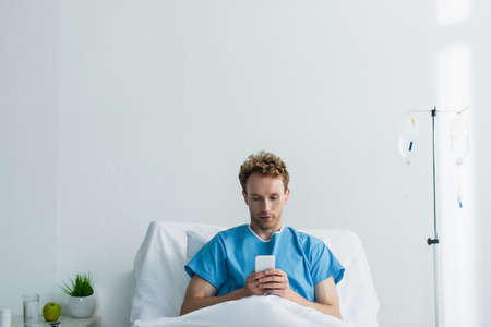 curly patient using smartphone while resting in hospital bedの写真素材