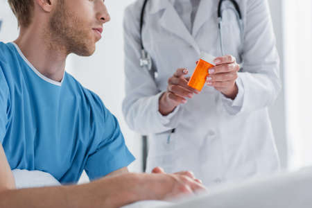 cropped view of doctor in white coat holding bottle with medication near patientの写真素材