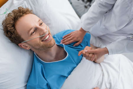 high angle view of doctor holding hand of smiling patient with nasal cannulaの写真素材