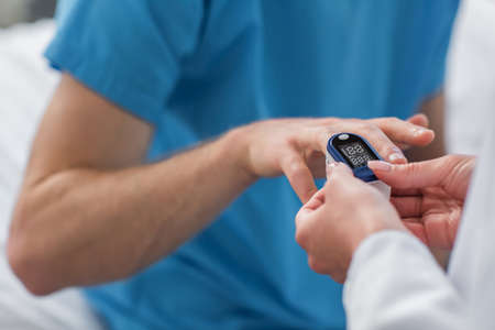 cropped view of doctor placing pulse oximeter on finger on patient in hospitalの写真素材