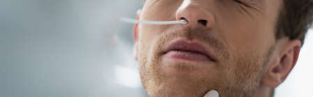cropped view of doctor holding swab near nose of patient while doing pcr test, bannerの写真素材