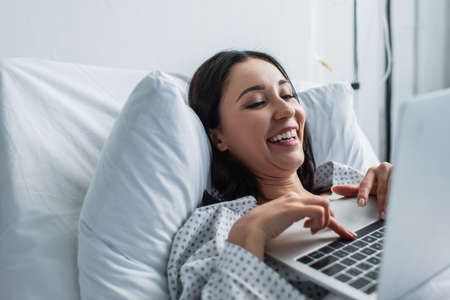 cheerful woman watching comedy movie on laptop in hospital bedの写真素材