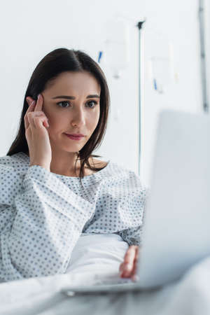 brunette freelancer looking at blurred laptop in hospitalの写真素材