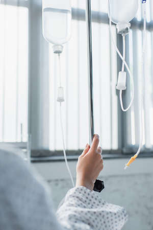 cropped view of sick woman holding hand on drop counter with intravenous therapy bottlesの写真素材