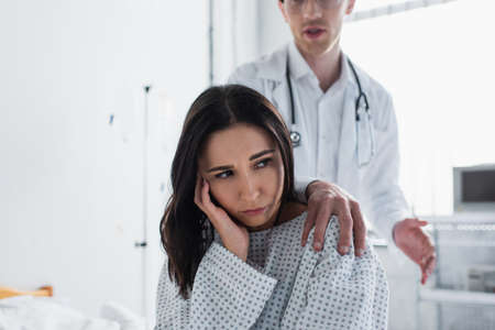 blurred doctor touching shoulder of upset patientの写真素材