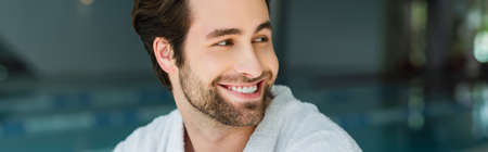 Smiling man in white bathrobe looking away in spa center, bannerの写真素材