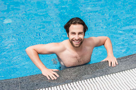 Happy man looking at camera in swimming pool during weekendの写真素材