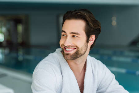 Cheerful man in white bathrobe looking away in spa centerの写真素材