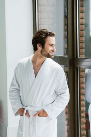 Cheerful man in white bathrobe looking at window in spa centerの写真素材
