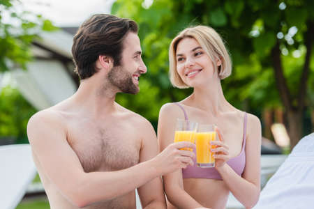 Smiling man clinking orange juice with girlfriend in swimsuit on resortの写真素材