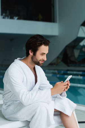 Man in bathrobe using mobile phone on deck chair in spa centerの写真素材